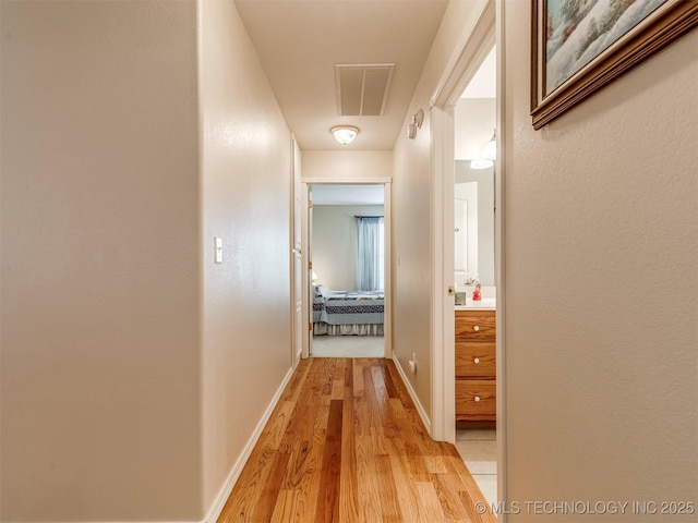 corridor featuring light wood-style flooring, visible vents, and baseboards