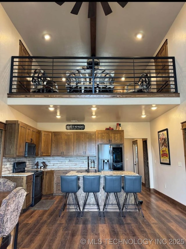 kitchen with a kitchen bar, a towering ceiling, stainless steel refrigerator with ice dispenser, and black / electric stove