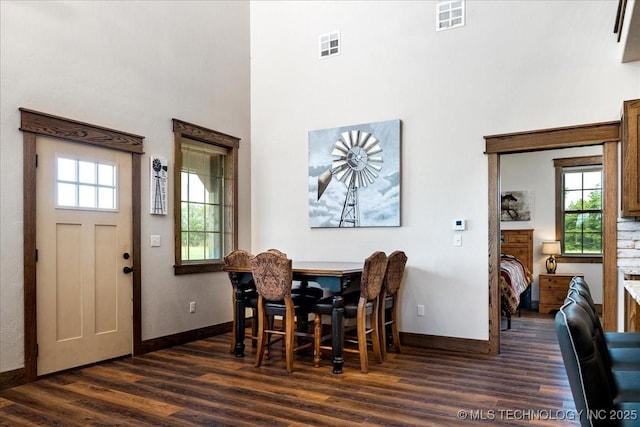 dining room featuring baseboards, a high ceiling, visible vents, and dark wood finished floors