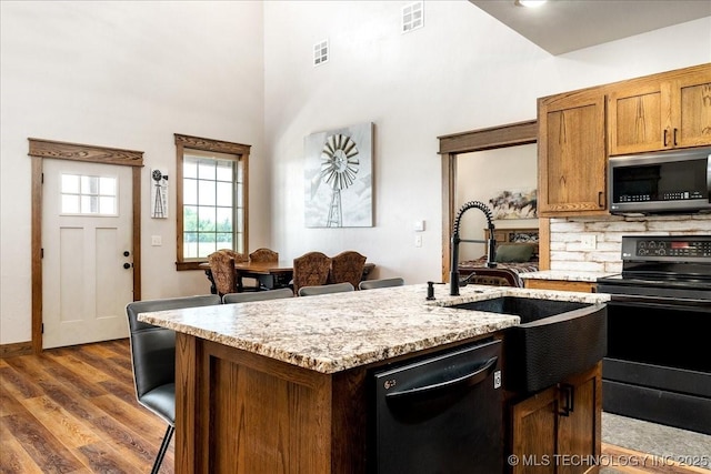 kitchen featuring dark wood-style flooring, a center island with sink, visible vents, a sink, and black appliances