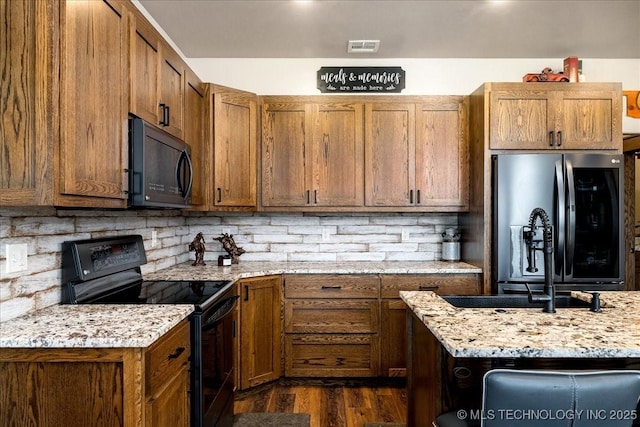 kitchen with dark wood-style floors, brown cabinets, backsplash, and black appliances