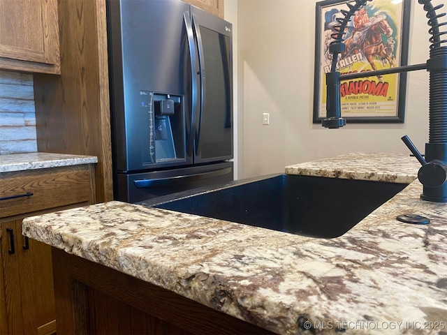 kitchen featuring brown cabinetry, stainless steel fridge, and light stone countertops