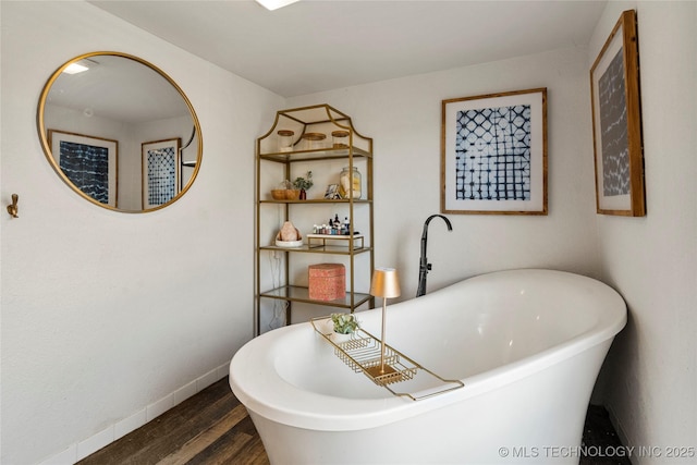 bathroom with a freestanding tub, wood finished floors, and baseboards