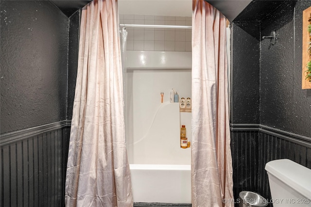 full bathroom with a textured wall, a wainscoted wall, shower / tub combo with curtain, and toilet