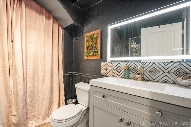 bathroom featuring toilet, curtained shower, vanity, and wainscoting