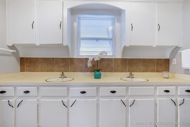 kitchen with light countertops, backsplash, a sink, and white cabinetry