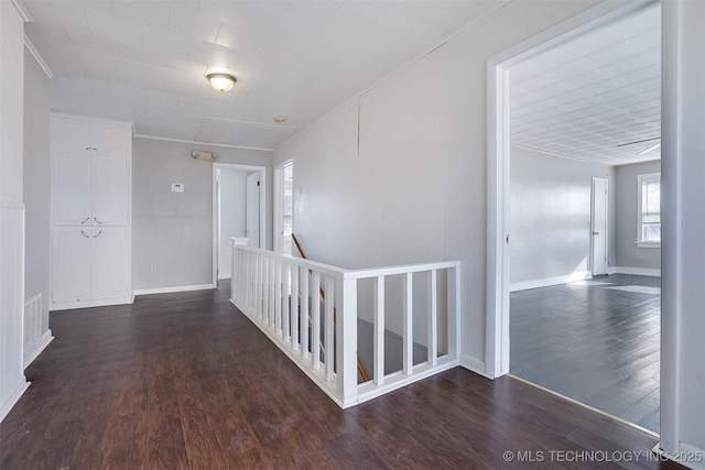 hallway featuring baseboards, visible vents, wood finished floors, crown molding, and an upstairs landing