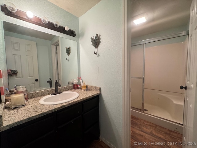 bathroom featuring a textured wall, a shower stall, vanity, and wood finished floors