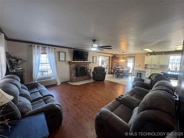 living room featuring a brick fireplace, ceiling fan, a textured ceiling, and wood finished floors