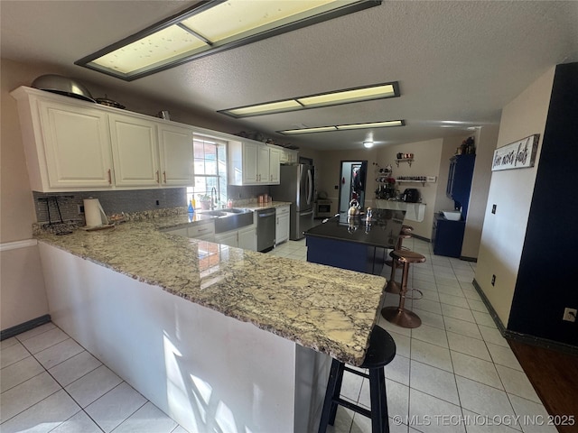 kitchen featuring stainless steel appliances, light tile patterned flooring, decorative backsplash, and a kitchen breakfast bar