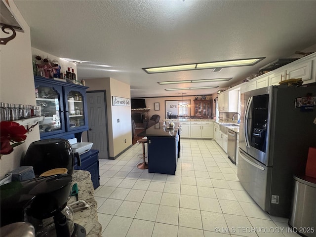 kitchen with white cabinets, light tile patterned floors, stainless steel appliances, and a textured ceiling