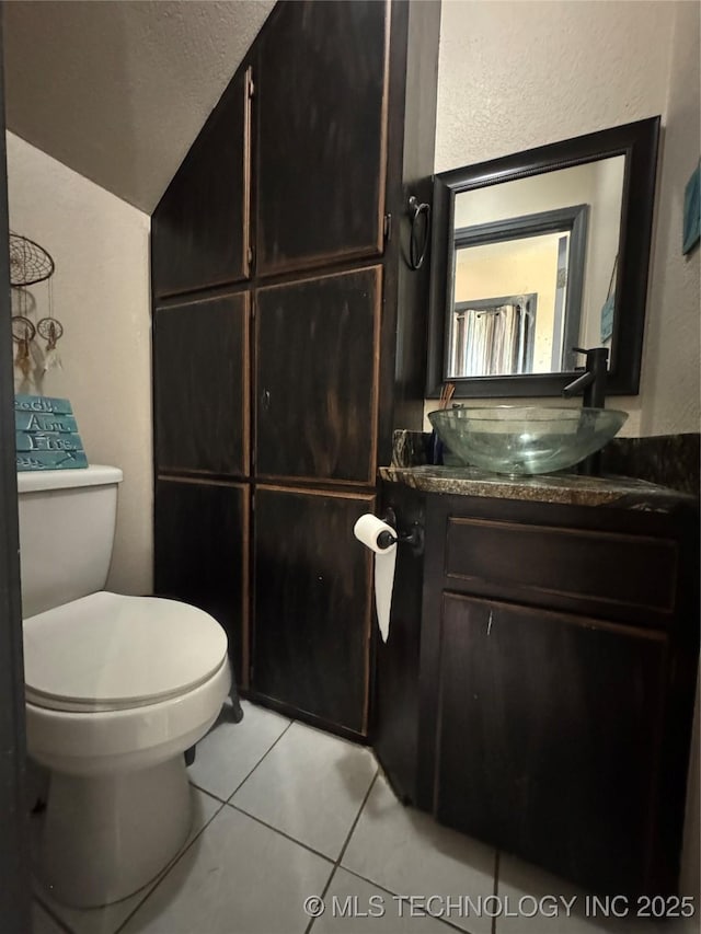 bathroom with a textured wall, toilet, vaulted ceiling, vanity, and tile patterned floors