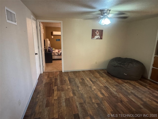 unfurnished room with a wall mounted air conditioner, visible vents, dark wood finished floors, and a textured ceiling