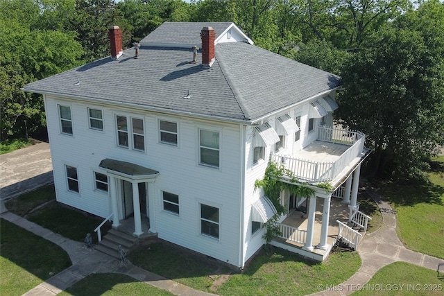 exterior space featuring roof with shingles, a chimney, a front yard, and a balcony