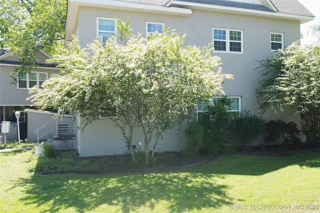 view of home's exterior with a yard, roof with shingles, and stucco siding