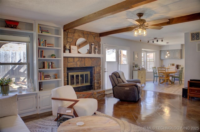 living area featuring ceiling fan, a textured ceiling, beamed ceiling, and a stone fireplace