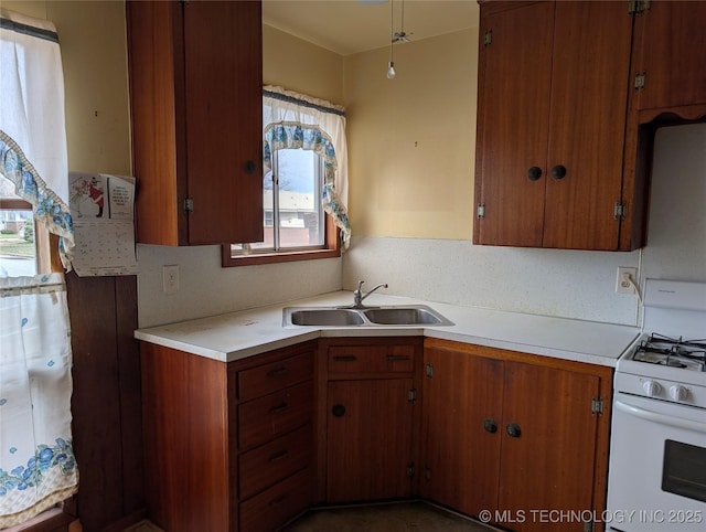 kitchen featuring light countertops, brown cabinetry, a sink, and white range with gas cooktop