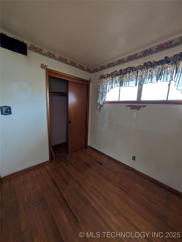 unfurnished bedroom with a closet, wood-type flooring, and baseboards