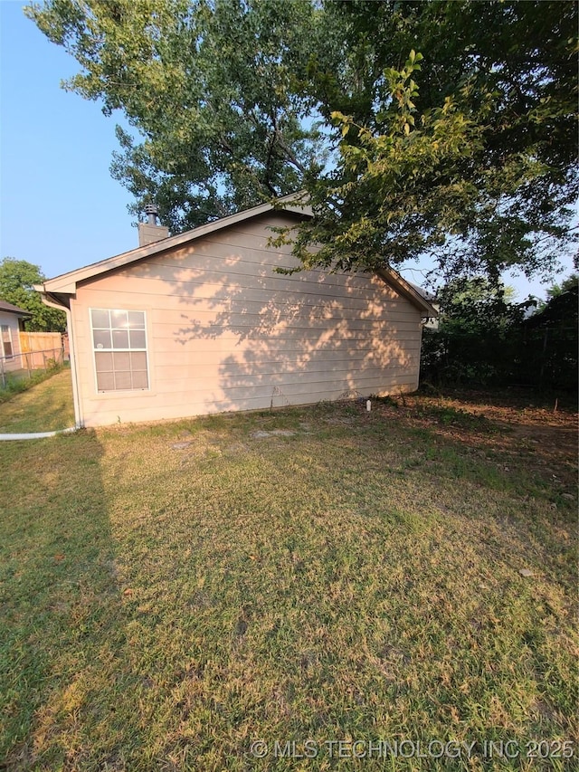 view of side of home featuring a lawn, a chimney, and fence