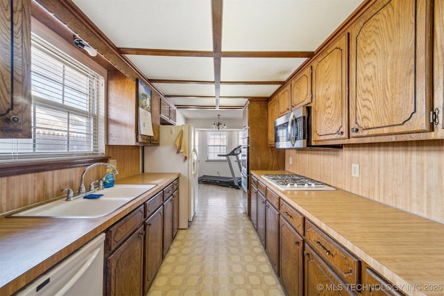 kitchen featuring white appliances, wooden walls, brown cabinets, light floors, and a sink