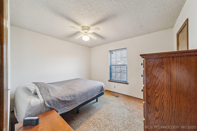 bedroom with light carpet, a textured ceiling, visible vents, and a ceiling fan