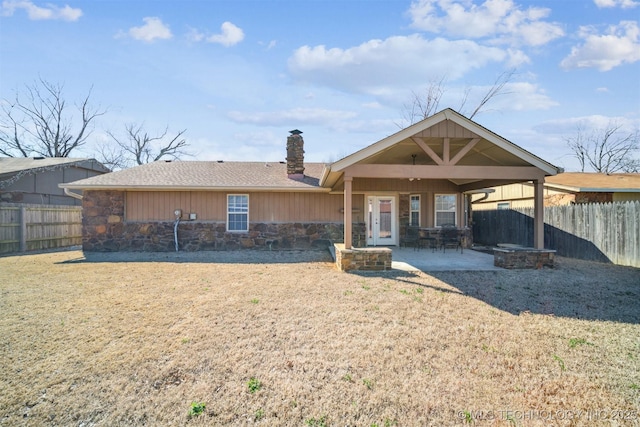 back of property with stone siding, a fenced backyard, and a chimney