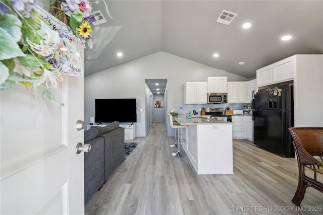 kitchen featuring visible vents, white cabinets, stainless steel appliances, light wood-style floors, and a kitchen bar