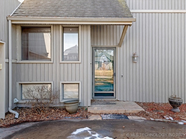 view of exterior entry with roof with shingles