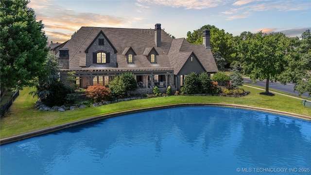 pool at dusk featuring a lawn and a pergola