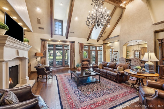 living area featuring a warm lit fireplace, arched walkways, wood finished floors, beam ceiling, and a notable chandelier