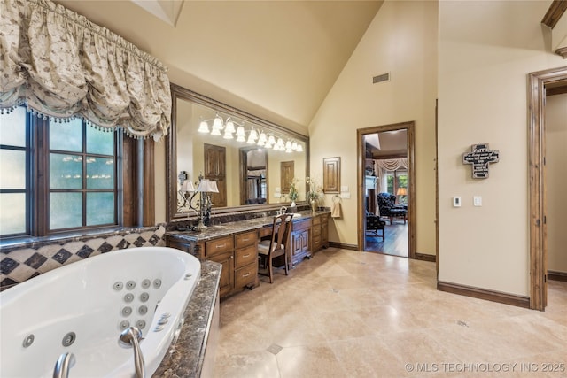 bathroom featuring visible vents, vanity, high vaulted ceiling, a jetted tub, and baseboards