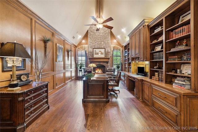 home office featuring a fireplace, built in desk, a decorative wall, dark wood-type flooring, and a ceiling fan