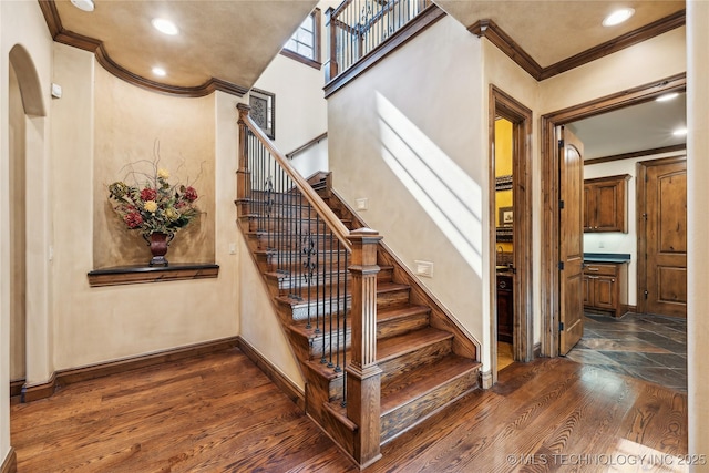 stairs with baseboards, ornamental molding, arched walkways, and wood finished floors