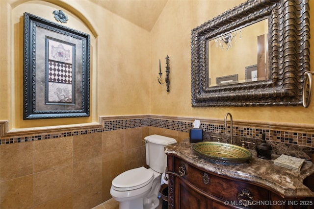 half bathroom featuring a wainscoted wall, vanity, toilet, and tile walls