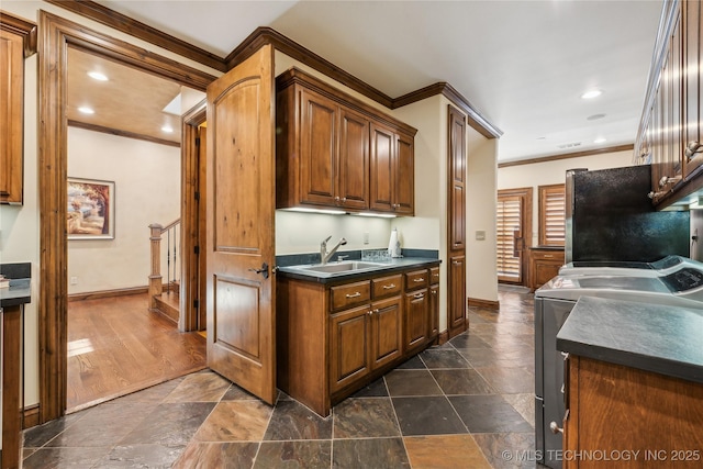 kitchen featuring washing machine and clothes dryer, dark countertops, ornamental molding, freestanding refrigerator, and a sink