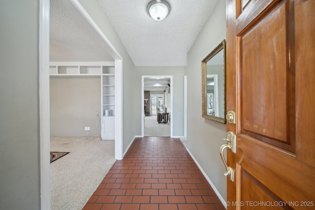 entryway featuring baseboards, a textured ceiling, dark tile patterned floors, and dark carpet