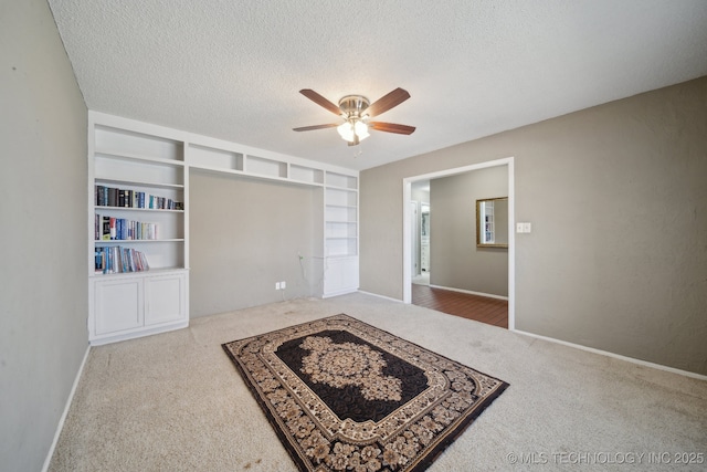 carpeted spare room featuring baseboards, built in features, a textured ceiling, and ceiling fan