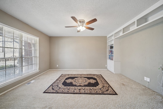 spare room with built in features, carpet, visible vents, ceiling fan, and a textured ceiling