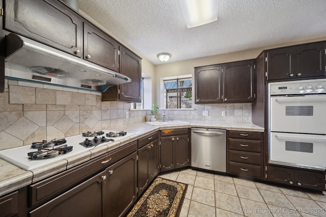 kitchen with white appliances, tile countertops, a sink, dark brown cabinetry, and under cabinet range hood