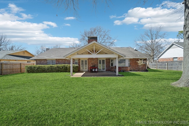 back of property with a lawn, a fenced backyard, french doors, brick siding, and a chimney