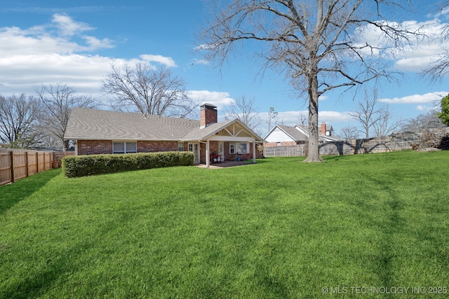 back of property featuring a chimney, a fenced backyard, brick siding, and a lawn