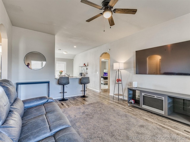 living room with arched walkways, ceiling fan, wood finished floors, and baseboards