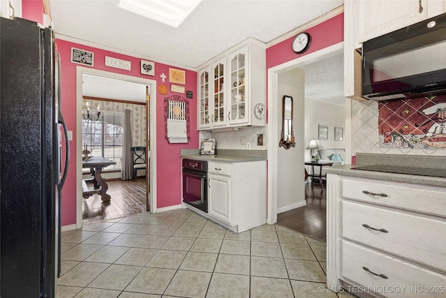 kitchen featuring light tile patterned flooring, white cabinets, light countertops, black appliances, and glass insert cabinets