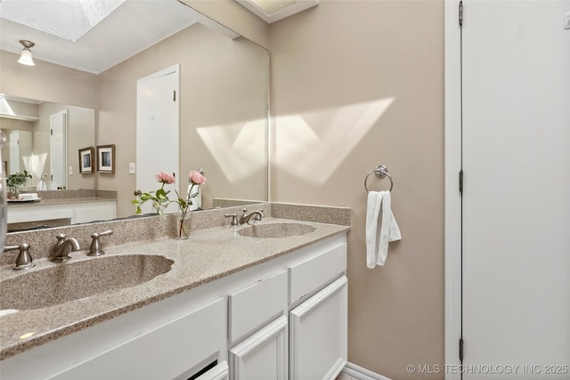 full bathroom featuring a skylight, a sink, baseboards, and double vanity