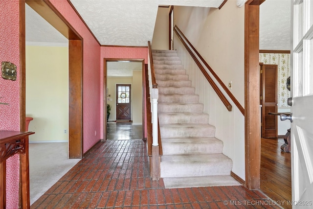 staircase with a textured ceiling, ornamental molding, brick floor, and wallpapered walls