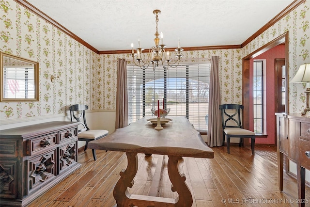 dining area with crown molding, hardwood / wood-style floors, a notable chandelier, and wallpapered walls