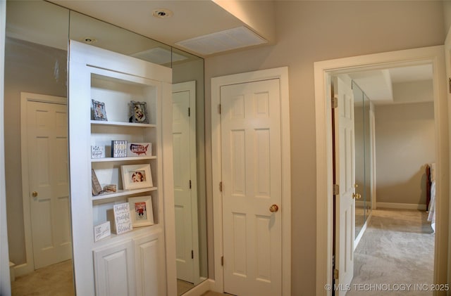 hallway featuring built in shelves, light colored carpet, and visible vents