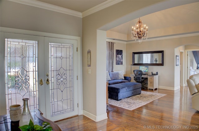 foyer with wood finished floors, arched walkways, a notable chandelier, and ornamental molding