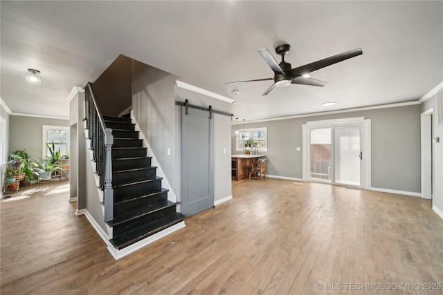 unfurnished living room with ornamental molding, a barn door, stairway, and wood finished floors