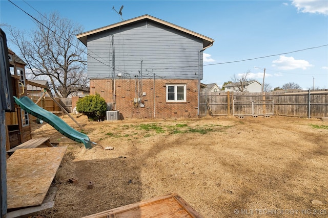 rear view of house featuring a fenced backyard, cooling unit, a playground, and brick siding